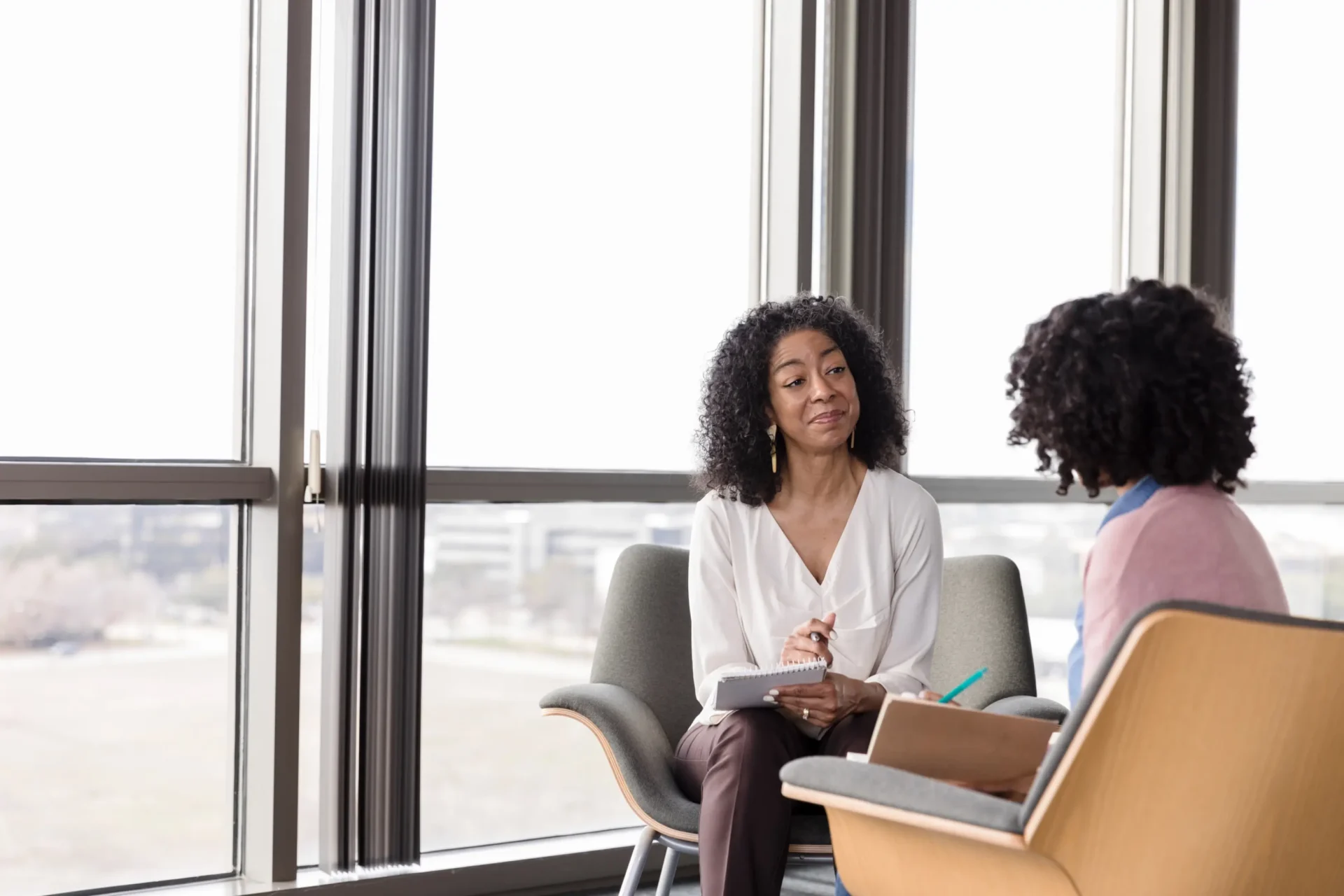 Two women engaged in a friendly conversation in a bright office.